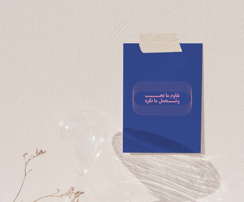 Pu&ograve; includere: Un biglietto blu con testo rosa che dice "شاوم ما نحب ونستعمل ما نكره". Il biglietto &egrave; attaccato a un muro bianco.
