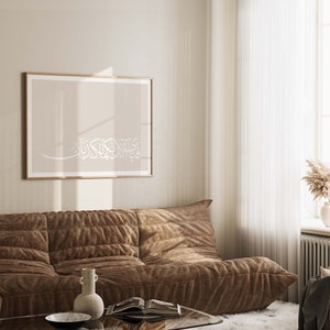 May include: A brown sofa against a beige wall with a framed print featuring white Arabic calligraphy on a beige background.