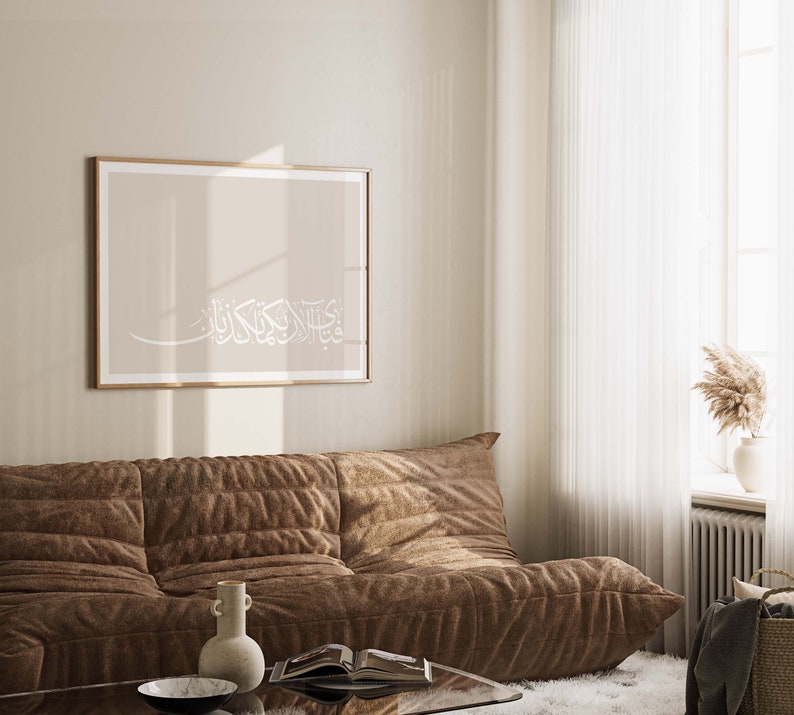 May include: A brown sofa against a beige wall with a framed print featuring white Arabic calligraphy on a beige background.