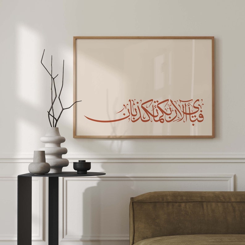 May include: A framed print with a brown wooden frame and a white background. The print features a red Arabic calligraphy inscription.