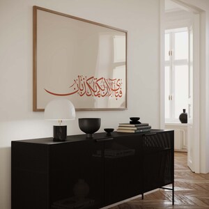 May include: A black metal cabinet with a mesh front and two doors. The cabinet is sitting on a wooden floor. A framed print with Arabic calligraphy hangs on the wall above the cabinet. A lamp and decorative bowls are on top of the cabinet.