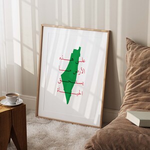 May include: A framed print with a green outline of the country of Palestine. The Arabic words "Palestine", "Free", "My", "Land", "On", "You", and "Palestine" are written in red inside the outline.