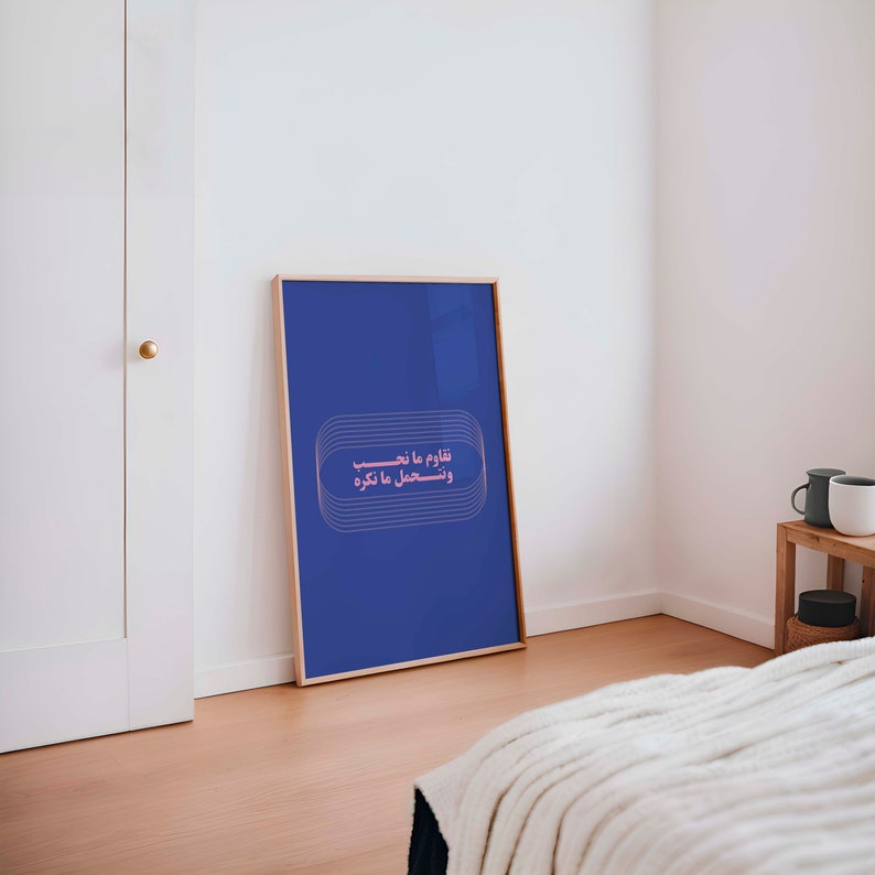 Pu&ograve; includere: Una stampa incorniciata con sfondo blu e testo arabo rosa che dice "قلوب ما تنسى و تسعد ما غرقت".