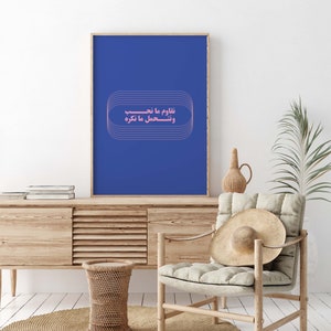 Pu&ograve; includere: Un poster incorniciato blu con una citazione araba rosa che recita "Impariamo da ci&ograve; che sperimentiamo e sperimentiamo ci&ograve; che impariamo." Il poster &egrave; appeso a un muro bianco sopra un mobile in legno.