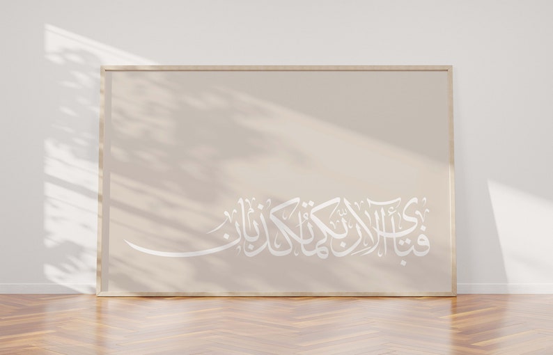 May include: A framed print with a beige background and white Arabic calligraphy. The calligraphy reads "فِي ظِلِّ الْعَرْشِ", which translates to "In the shade of the Throne".