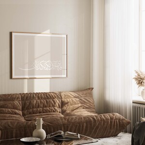 May include: A brown couch with a beige wall and a framed print with Arabic calligraphy in white on a beige background.