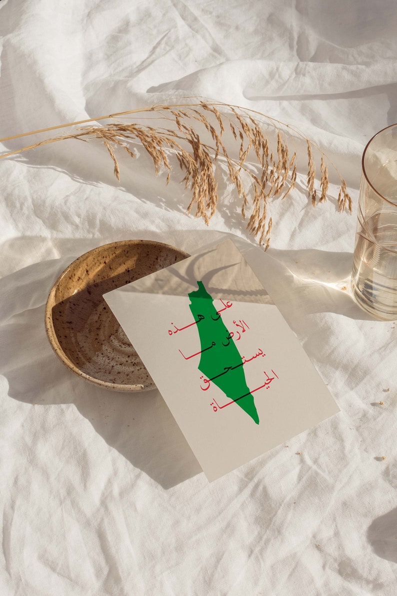 May include: A white card with a green outline of the country of Palestine. The Arabic words "Palestine" and "Jerusalem" are written in red on the card.