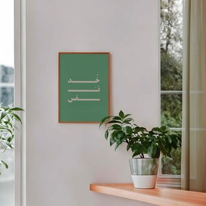Puede incluir: Una impresi&oacute;n enmarcada con fondo verde y caligraf&iacute;a &aacute;rabe blanca. La caligraf&iacute;a dice "خير", que se traduce como "bondad". La impresi&oacute;n est&aacute; colgada en una pared blanca con una planta en maceta delante.