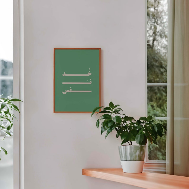 Puede incluir: Una impresi&oacute;n enmarcada con fondo verde y caligraf&iacute;a &aacute;rabe blanca. La caligraf&iacute;a dice "خير", que se traduce como "bondad". La impresi&oacute;n est&aacute; colgada en una pared blanca con una planta en maceta delante.