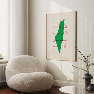May include: A white framed poster with a green outline of the country of Palestine. The poster has Arabic text in red that reads "Upon the land, the right, the resistance, the liberation".