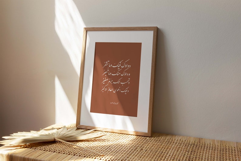 May include: A framed print with a brown background and white calligraphy in Arabic script. The text reads "دو اوک فیک و ما تشعر و دارک منگ و ما تبصر تحب ایک جرم صغیر ونيك العلوي العالم الاكبر".