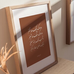 May include: A framed print with a brown background and white Arabic calligraphy. The text reads "Two good deeds are better than a thousand prayers." The print is in a light wood frame and is sitting on a wooden surface.