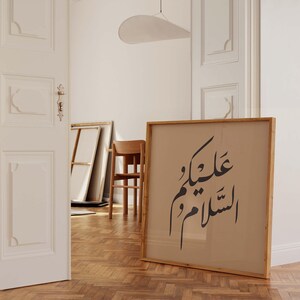 May include: A framed print with Arabic calligraphy in black ink on a beige background. The frame is made of natural wood and has a light brown finish.