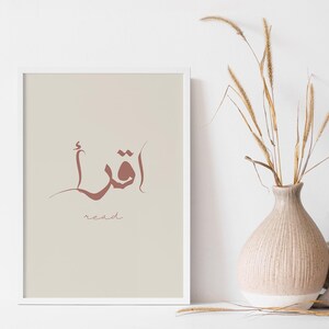 Puede incluir: Una impresi&oacute;n enmarcada blanca con un fondo beige. La impresi&oacute;n presenta la palabra &aacute;rabe para "leer" en caligraf&iacute;a marr&oacute;n. La palabra "leer" est&aacute; escrita en ingl&eacute;s debajo de la palabra &aacute;rabe.