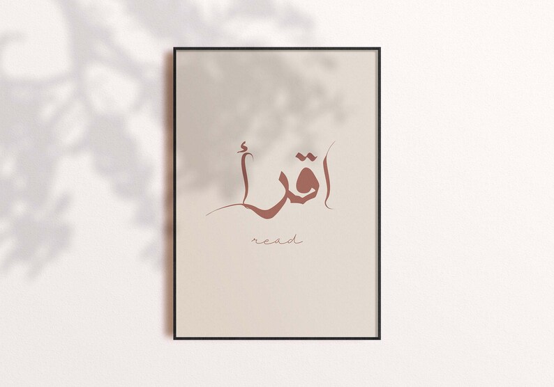 Puede incluir: Una impresi&oacute;n enmarcada con un dise&ntilde;o de caligraf&iacute;a &aacute;rabe marr&oacute;n que dice "أقرأ", que se traduce como "leer" en ingl&eacute;s. El fondo es de color beige claro.