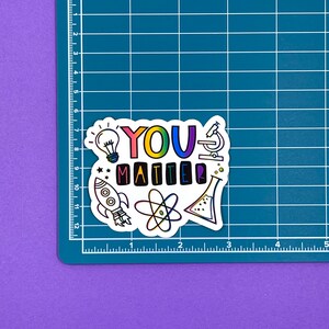 May include: A white sticker with the text "YOU MATTER" in rainbow colors. The sticker is decorated with colorful illustrations of a lightbulb, a rocket, an atom, a microscope, and a beaker.
