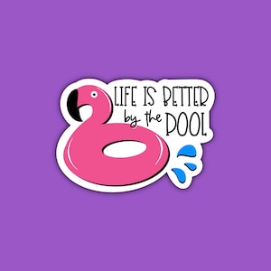 May include: A pink flamingo pool float with the text "Life is better by the pool" in black lettering. Blue water droplets are shown coming from the float.