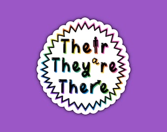 May include: A white sticker with a rainbow outline and a starburst shape. The sticker says "Their They're There" in black text.