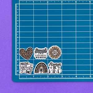 May include: Five leopard print themed stickers with various sayings. The stickers are on a blue grid background. The stickers say "Leopard is my favorite", "Stay Wild", "Positive Vibes Only", "Always Be Kind", and a heart with leopard print.