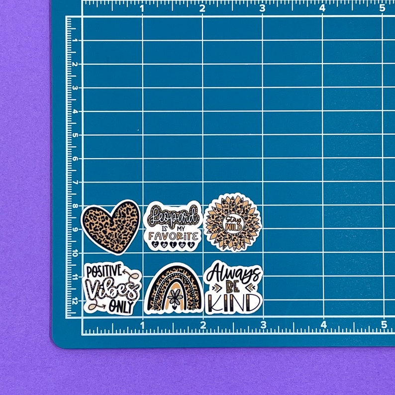 May include: Five leopard print themed stickers with various sayings. The stickers are on a blue grid background. The stickers say "Leopard is my favorite", "Stay Wild", "Positive Vibes Only", "Always Be Kind", and a heart with leopard print.