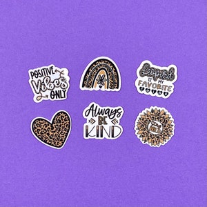 May include: Six leopard print stickers with different sayings. The stickers include "Positive Vibes Only", "Leopard is my Favorite Color", "Always Be Kind", "Stay Wild", and a rainbow with a flower.