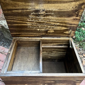 Puede incluir: Una caja de madera para recuerdos con una tapa con bisagras. La tapa est&aacute; abierta y presenta un mensaje grabado: "Remember my sweet girl, you are the universe. Your energy is magnetic. What you think you become. You are my most precious gift. I love you through all of time. Mama." La caja est&aacute; cerrada y tiene el nombre "Lillian" grabado en la parte delantera.