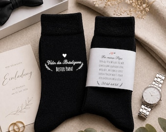 May include: A pair of black socks with white text, one reading "Vater des Bräutigams, BESTER PAPA!" and the other with a message for "Papa". Also, a wedding invitation, a bow tie, a watch, and cufflinks are visible.