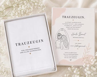 May include: A white gift box with a folded white cloth inside, and a matching box with text and illustrations. The text on the cloth reads "TRAUZEUGIN" and "FÜR FREUDENTRÄNEN UND ALLES DAZWISCHEN." The other box has text and a drawing of two women.