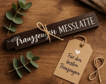 May include: A brown wooden folding ruler with the text "Trauzeugen Messlatte" and a brown paper tag with the text "Für den besten Trauzeugen" and a white heart.