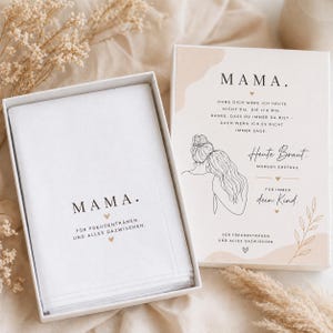 Puede incluir: Un juego de caja de regalo blanco con un pañuelo a juego. El pañuelo y la tapa de la caja presentan la palabra "MAMA" en texto negro. La tapa de la caja también tiene un dibujo lineal de dos mujeres y texto adicional.