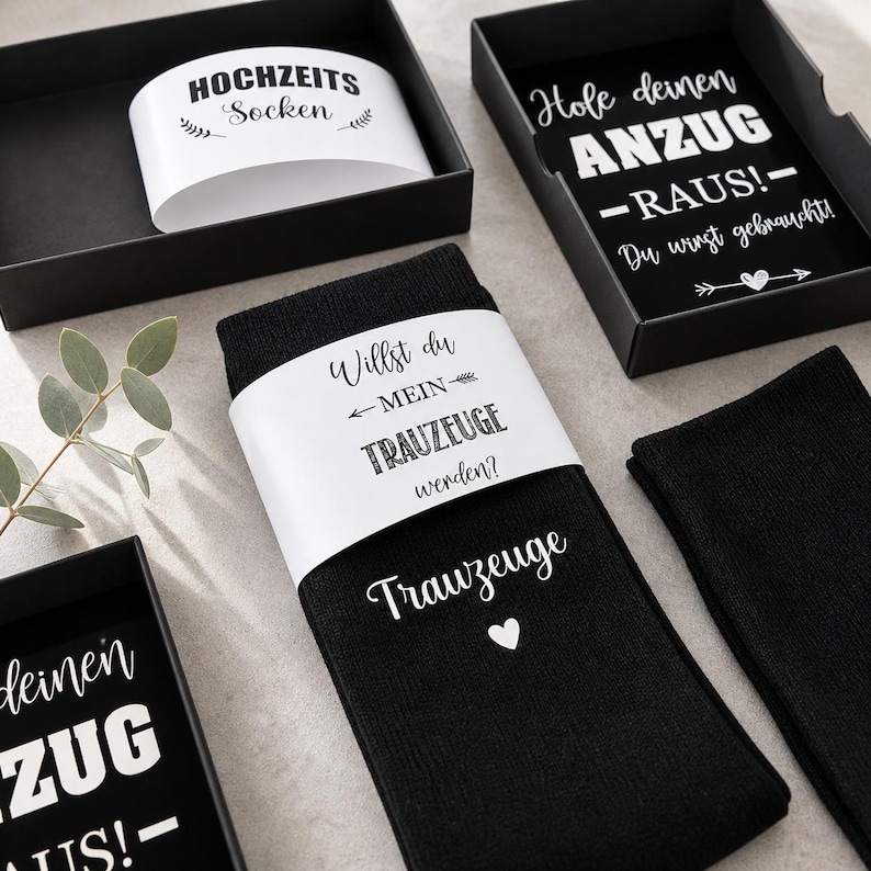 May include: Black socks with white text reading "Willst du MEIN TRAUZEUGE werden?" and "Trauzeuge" with a heart. The socks are packaged in a black box with the text "HOCHZEITS Socken". Another box has the text "Hole deinen ANZUG -RAUS!"