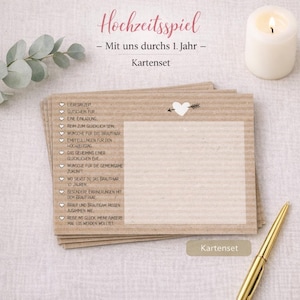 Könnte beinhalten: Ein Stapel Karten aus Kraftpapier mit dem deutschen Text "Hochzeitsspiel" und "Kartenset". Die Karten haben ein Herz- und Pfeildesign, mit einem goldenen Stift und einer brennenden Kerze im Hintergrund. Die Karten sind für eine Hochzeit.