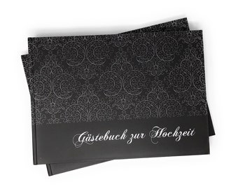 May include: Black guest book with a silver floral pattern and the text "Guestbook for the Wedding" in silver lettering.