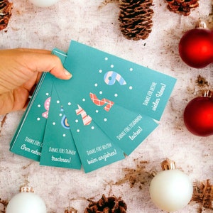 May include: A set of teal blue cards with white polka dots and red and white striped numbers. Each card has a different message in German, such as "Danke f&uuml;rs Tr&auml;nnen trocknen!" (Thanks for drying tears!) and "Danke f&uuml;rs zusammen lachen!" (Thanks for laughing together!).