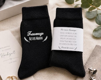 May include: Black socks with white text reading "Trauzeuge Bester Mann" and a sprig design. A second sock has a white label with German text. Wedding theme with rings, bow tie, and invitation.