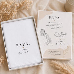 May include: A white gift box with the word "PAPA" printed in black, and the words "Für immer dein Kind" in a script font. The box contains a folded white cloth. A second box has text and a drawing of a couple.