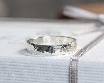 May include: A silver hammered band ring. The ring is thick and has a textured surface.