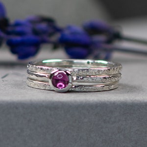 May include: A silver ring with three bands and a pink gemstone in the centre. The bands have a textured finish.