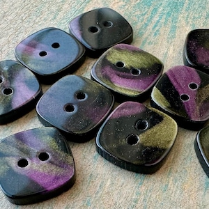 May include: Ten square-shaped buttons with two holes each. The buttons are black with iridescent purple and gold swirls.