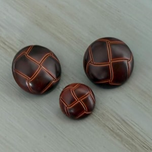 May include: Three dark brown buttons with a stitched pattern. The buttons vary in size, with the largest measuring approximately 1.5 inches in diameter and the smallest about 0.75 inches. The buttons have a glossy finish.