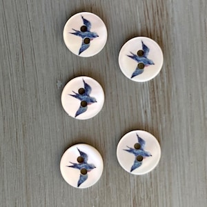 May include: Five white round buttons with a blue swallow design. The buttons have two holes.