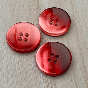 May include: Three red plastic buttons with four holes each. The buttons have a gradient color effect, fading from a darker red to a lighter red.