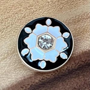 May include: A round, black and white enamel pin with a white snowflake design and a clear rhinestone in the center.