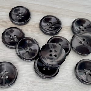 May include: A collection of ten black plastic buttons with five holes each. The buttons are round and have a glossy finish.