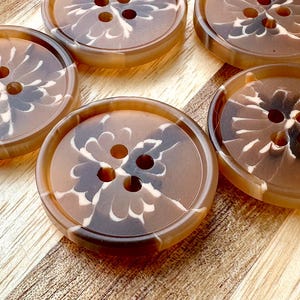 May include: Four brown and white patterned buttons with four holes each. The buttons have a swirl design and are made of a smooth, shiny material.