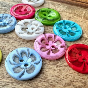 May include: Assortment of colorful buttons with a floral design. The buttons are made of plastic and have a glossy finish. The colors include red, pink, blue, green, white, and yellow.