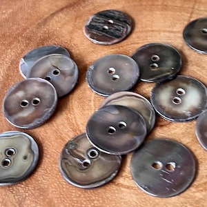 May include: A collection of brown and white shell buttons with two holes each. The buttons are arranged in a random pattern on a wooden surface.