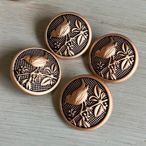 May include: Four bronze-colored buttons with a bird perched on a branch design. The buttons are round with a textured background and a detailed bird and leaf motif. The buttons are approximately 1 inch in diameter.