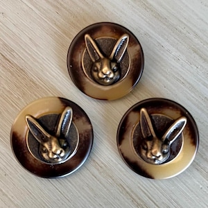 May include: Three brown and beige round buttons with a raised metal bunny rabbit design. The buttons have a mottled brown and beige pattern.
