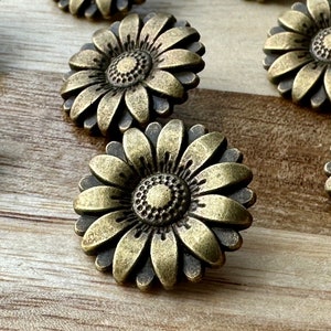 May include: A set of 10 antique gold-toned metal daisy flower buttons. Each button features a raised, detailed daisy design with a textured center.